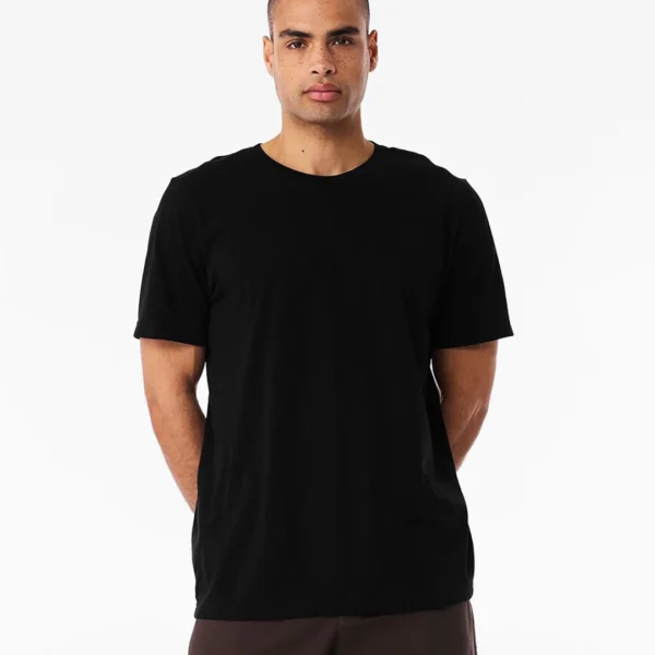 Man wearing a plain black short-sleeve t-shirt; hands behind his back against a white studio background.
